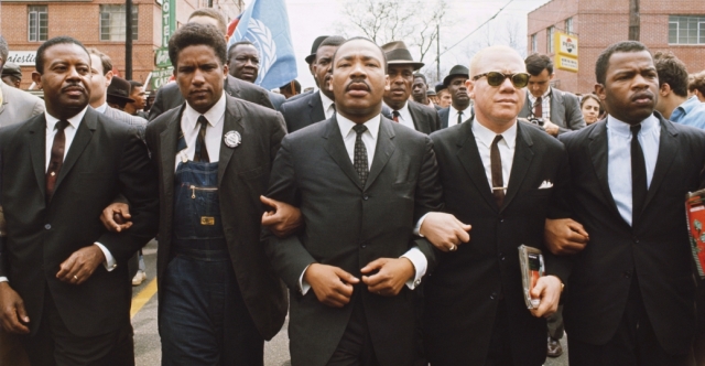 James Forman (blazer/overalls) locks arms with MLK as they enter Montgomery, 1965.